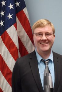 A portrait of a man with an American flag in the background.